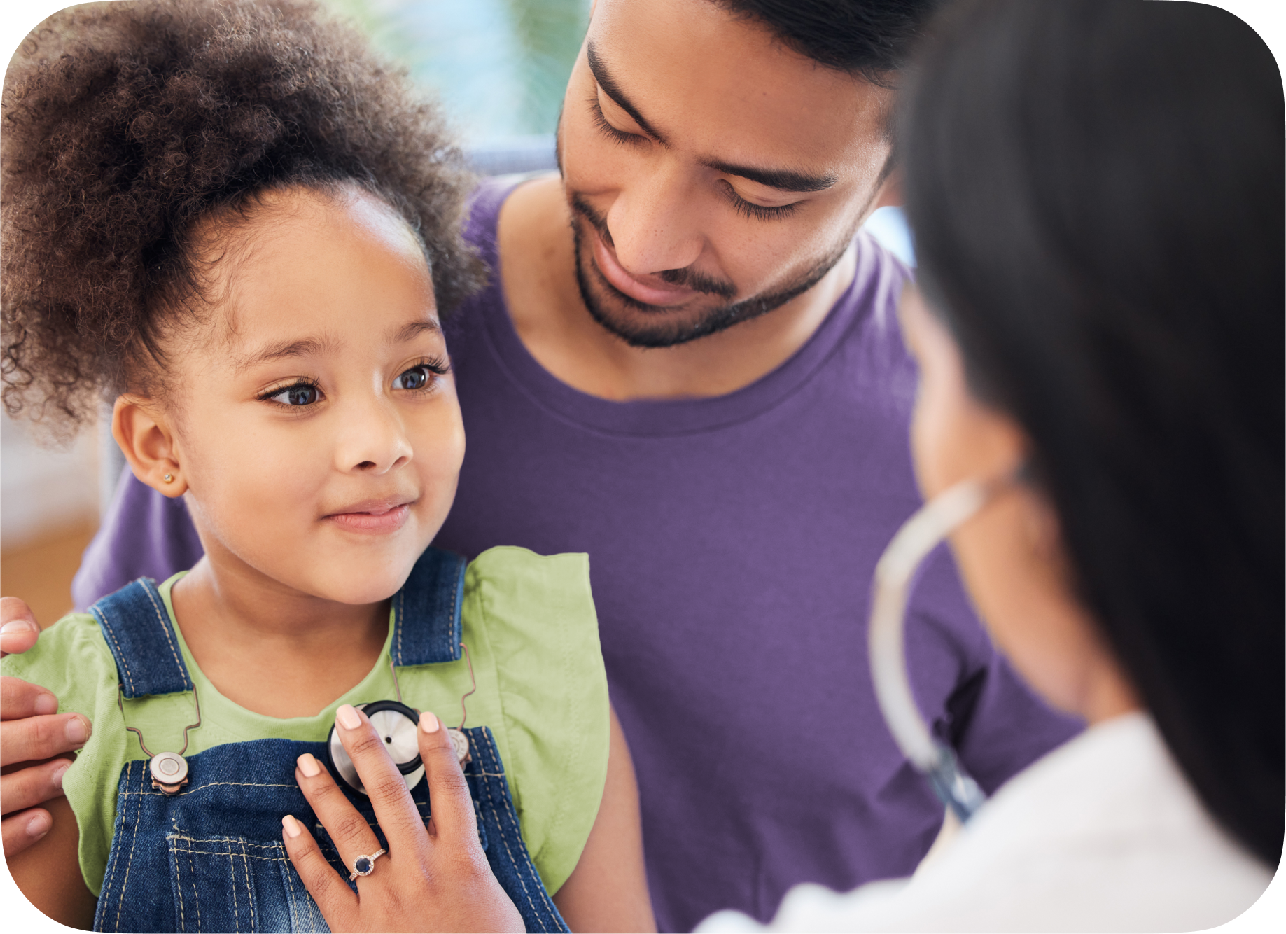 Little girl getting a check-up with a physician while sitting on her father's lap.